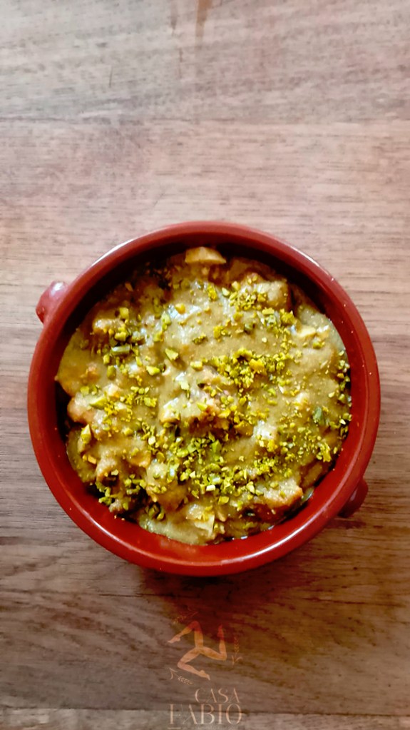 Un plat de dessert crémeux garni de pistaches hachées, servi dans un bol en terre cuite.